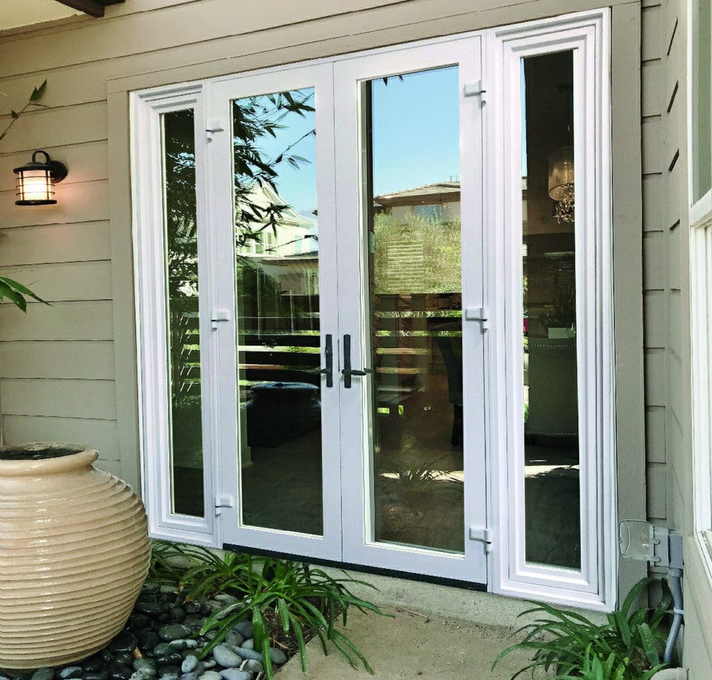 Win-Dor(swing) Glass double doors with white frames open to a bright interior, flanked by narrow windows. There's a large beige planter with greenery next to the door and a black wall lantern on the side.